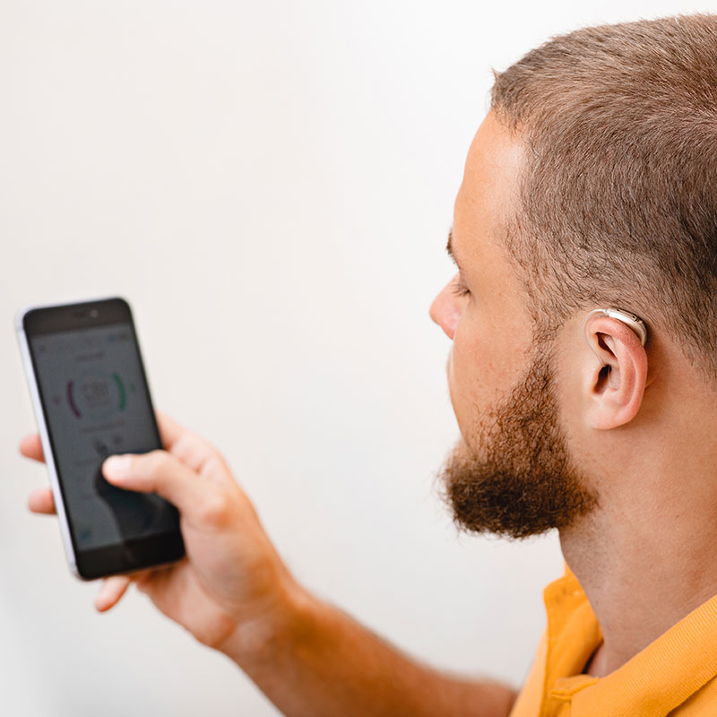 A man adjusts the settings on his hearing aid using a smartphone app